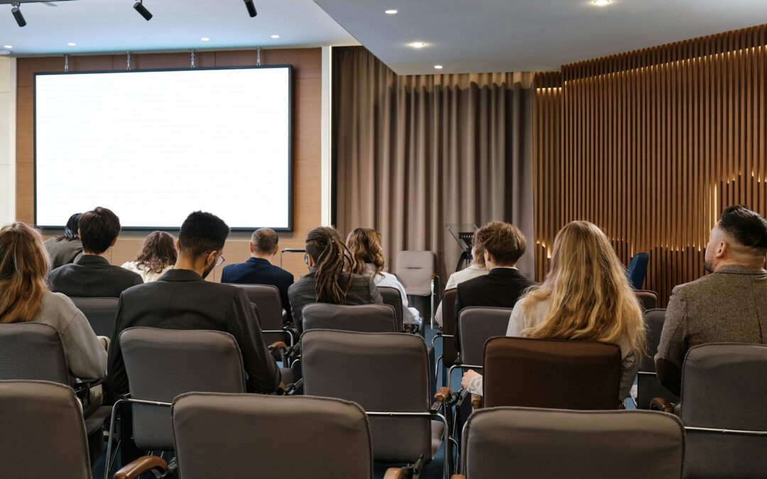 Conference attendees sitting in auditorium with a screen in the front